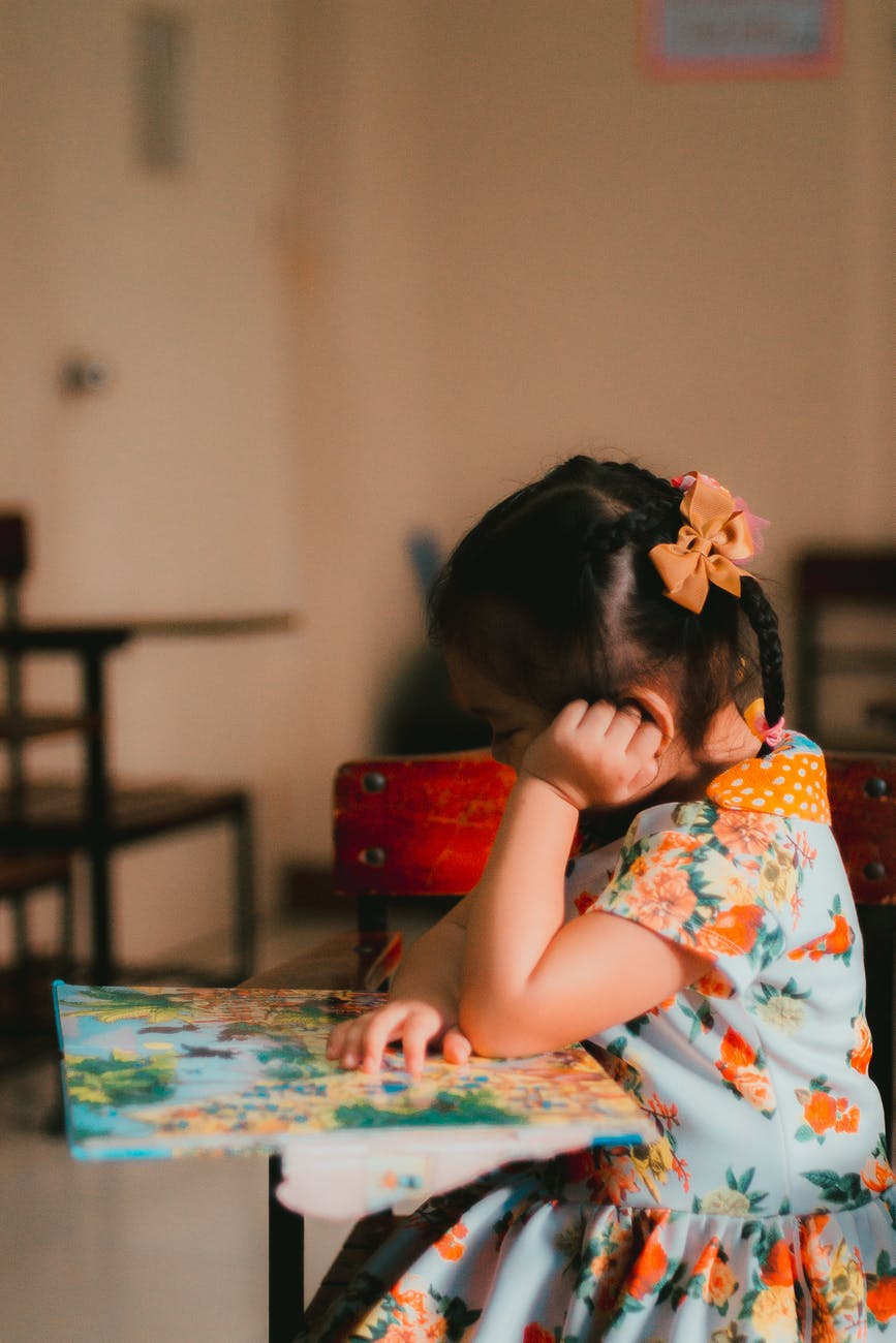 A young girl rests her cheek on her hand while looking at a book in deep concentration.