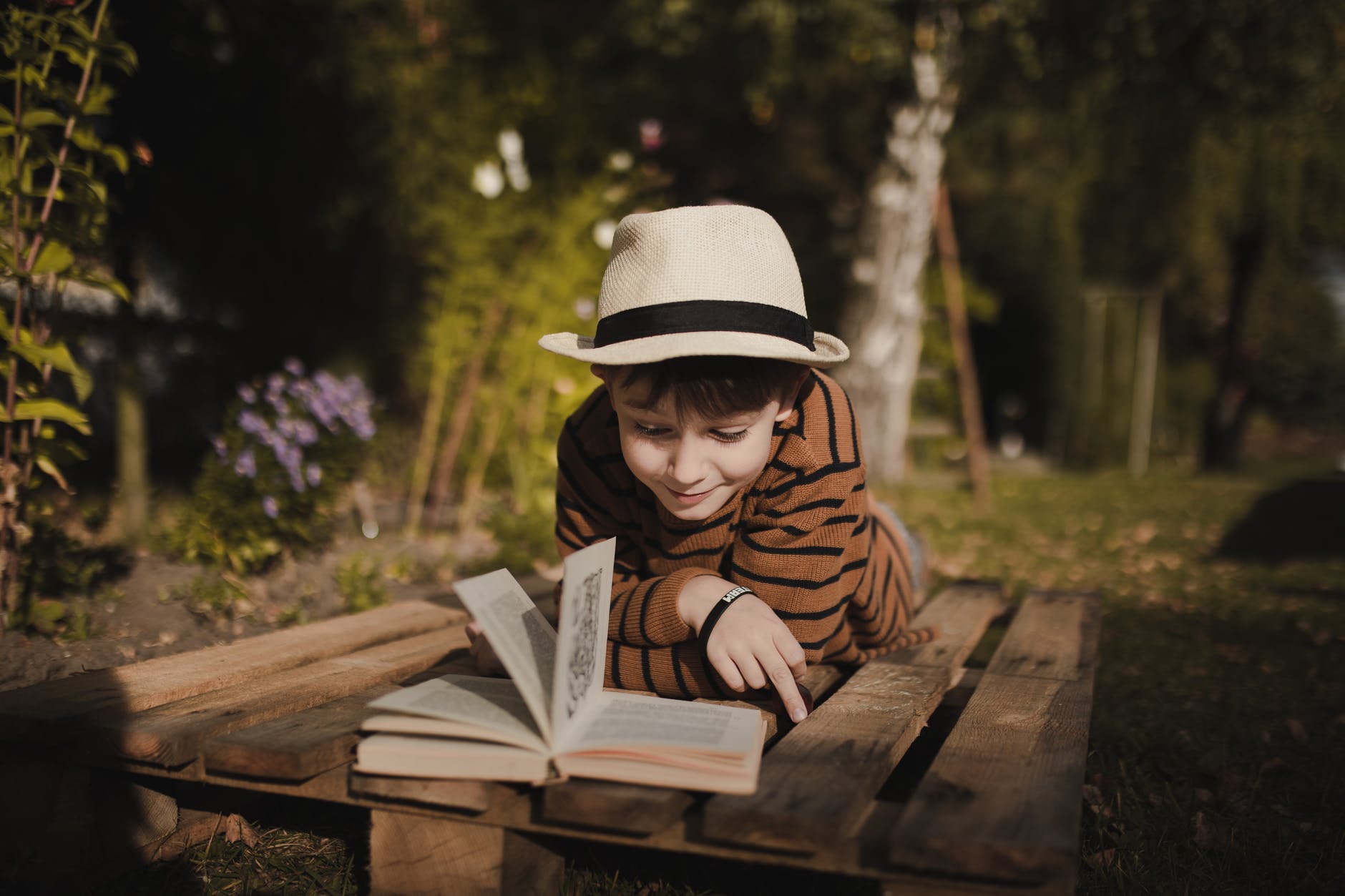 smiling boy reading book on bench in park