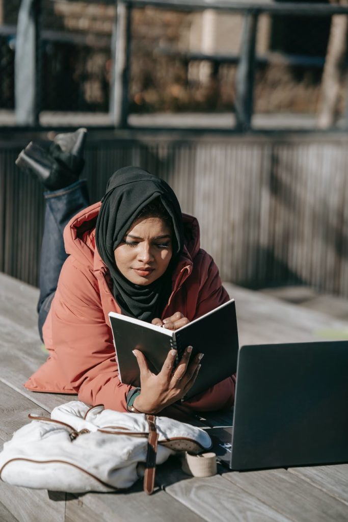 A Muslim woman reads a book outdoors. From her expression, she seems a little confused about what's going on in the book.